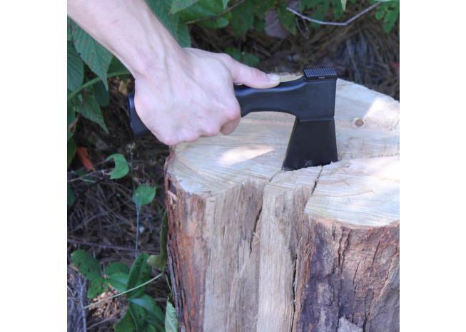 Hand holding a black axe over a wooden log with a natural background