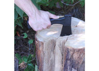 Hand holding a black axe over a wooden log with a natural background