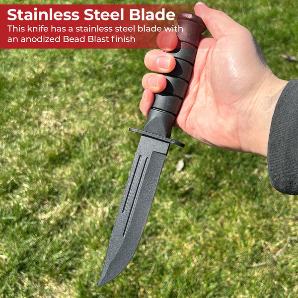Hand holding a knife with a stainless steel blade and anodized Bead Blast finish against a grassy background.